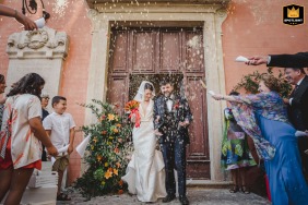 Celebrating their wedding at Castello di Modanella, Tuscany, the happy couple exits the venue immediately following the ceremony while smiling guests excitedly toss handfuls of celebratory confetti into the air.